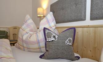 A cozy bedroom with large pillows and a decorative sheep-themed pillow. The walls are bright and warmly lit.