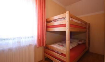 A cozy room with a bunk bed in warm colors. Light curtains hang in front of the window, allowing the light to come in.