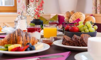 A rich breakfast buffet with croissants, fresh fruits, and various drinks. Rolls and desserts are also arranged on the table.