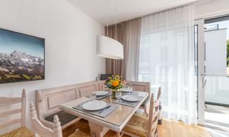 An elegant dining area with a wooden chair set and a glass table. Generous windows provide plenty of light and a beautiful view outside.