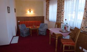 A cozy room with a small table and chairs. The carpet is red, and there are large windows with curtains.