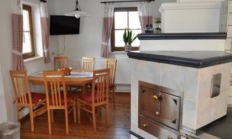 A cozy kitchen with a round dining table and wooden chairs. The room has a warm atmosphere with a beautiful stove and windows with curtains.