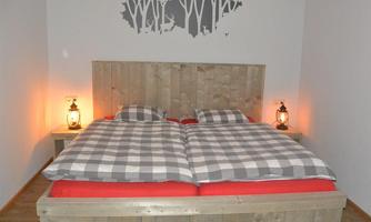 A cozy bedroom with a large wooden bed and checkered bedcovers. Soft lighting from two lanterns creates an inviting atmosphere.