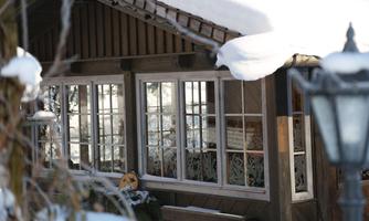 A cozy cabin in winter with snow on the roof. The windows display a calm, inviting atmosphere.