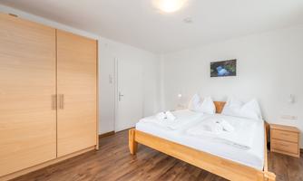 A cozy bedroom with a double bed and bright bedding. The room features a wooden cabinet and a modern look.