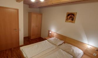 A simple and modern bedroom with a double bed and bright wood details. The walls are in neutral colors, and there is a wardrobe as well as a piece of artwork above the bed.