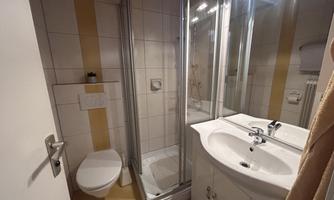 A modern bathroom with a shower, a sink, and a toilet. The walls are brightly tiled and well-lit.