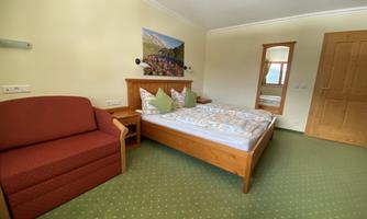 A cozy bedroom with a double bed and a red sofa. The walls are light, and there is a window with a view outside.