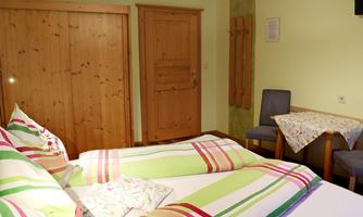 A cozy room with a double bed and colorful bedding. There is a table and chairs as well as a wooden door in the background.