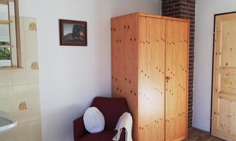 A simple room with a wooden wardrobe, a chair, and a mirror. The walls are light, and there is a picture on the wall.