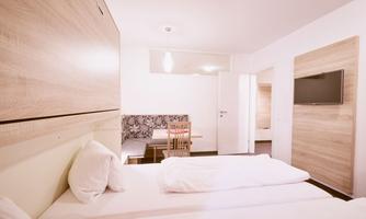 A bright and modern room with two single beds. There is a small table with chairs and a television on the wall.