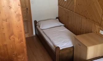 A simple room with two single beds. There is a wooden table and a wooden dresser.