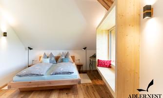 A modern bedroom with a large bed and wooden walls. Light streams through a window, creating a cozy atmosphere.