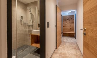 A modern bathroom with a glass shower and a sink is visible. The hallway has bright walls and wooden doors that create an inviting atmosphere.