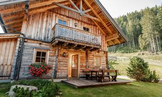 A cozy wooden house with a balcony and a lovely porch. The garden is well-maintained and surrounded by trees.