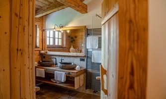 A modern bathroom with wooden accents and two sinks. Large windows provide plenty of natural light.