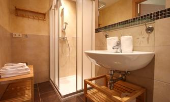 A modern bathroom with a shower and a washbasin. Towels are neatly placed on a wooden shelf and a bench.