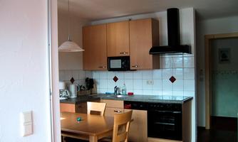 A modern kitchen with wooden cabinets and a dining table. There is a stove, a microwave, and kitchen appliances on the countertop.