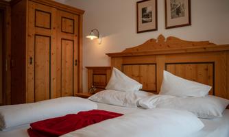 A cozy bedroom with a wooden cabinet and a double bed. White pillows and a red blanket give the room an inviting atmosphere.