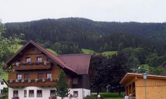 A traditional wooden house with flower boxes and a landscaped garden. In the background, majestic mountains and forests can be seen.