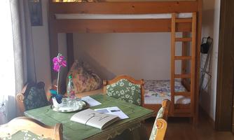 A cozy room with a bunk bed and a dining table. The decor is rustic and the windows bring in plenty of daylight.