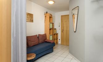A small entrance area with a blue sofa and a wooden stool. A mirror and a piece of art hang on the wall.