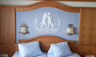 A cozy bedroom with a wooden headboard and two pillows. On the wall, there is a decorative relief sculpture and two bedside lamps.