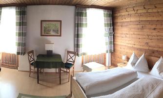 A cozy room with wooden paneling, two beds and a bunk bed. There is a table, chairs, and a television.