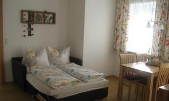 A cozy room with a sofa bed and a dining table. The walls are adorned with light curtains and beautiful decoration.