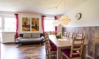 An inviting living and dining area with a large table and chairs. Large windows and modern lamps create a bright atmosphere.