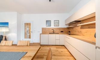 A modern kitchen with bright wood surfaces and white cabinets. The dining area is equipped with a large wooden table and simple chairs.