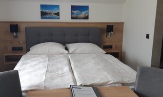 A cozy bedroom with a double bed and two chairs.  
On the wall hang two pictures of mountains.
