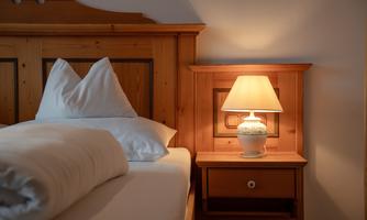 A cozy bedroom with a wooden bed and two pillows. A night lamp on a nightstand provides warm light.