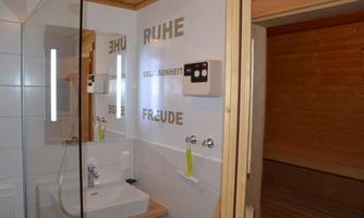 A modern bathroom with a sink, a large mirror, and stylish wall lights. The walls are decorated with positive words that create a relaxing atmosphere.