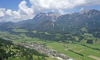 A beautiful landscape with mountains in the background and a small town in the foreground. Green meadows and clouds in the blue sky complement the picture.