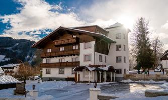 A cozy hotel with a traditional wooden balustrade stands in a snow-covered landscape. The mountains and the clear sky in the background give the place a picturesque atmosphere.