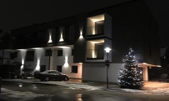 A modern building at night, illuminated by warm light. In front of the house stands a Christmas tree, festively decorated.