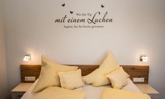 A cozy bedroom with a large bed that has many yellow pillows. On the wall, there is a saying that invites you to smile.