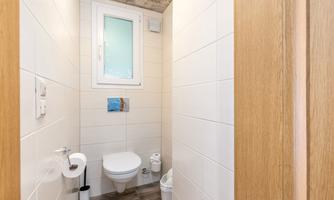 A modern bathroom with a light tiled floor and a window. There is a toilet and a trash can.