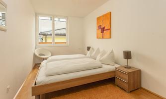 A cozy bedroom with two beds and bright walls. There is a large window, a carpet, and modern furniture.