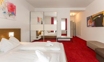 A modern hotel room with red carpet, white bedding, and a large mirror. Colorful artworks hang on the walls.
