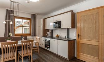 A modern kitchen with wooden furniture and a dining table. The window lets in plenty of daylight and the atmosphere is inviting.
