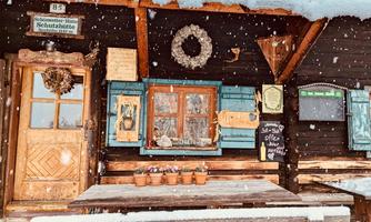 A rustic mountain cabin with wooden cladding and a large entrance. Outside, it is snowing, and blooming plants are on the table.