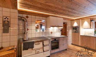 A modern kitchen with a wooden ceiling and elegant tiles. It is well equipped with a stove, an oven, and plenty of storage space.