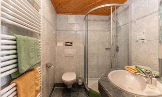 A modern bathroom with a shower and a sink. Towels in various colors are neatly hung.