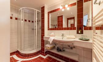 A modern bathroom with a shower cabin and a large mirror. The walls are decorated with white and red tiles.