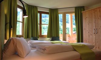 A bright room with two beds and green curtains. Large windows offer a view of the countryside.