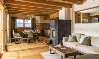 A stylish living room with wooden ceilings and a modern fireplace. A large dining table and cozy furniture create an inviting atmosphere.