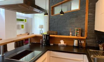 A modern kitchen with a cooktop, a kettle, and a coffee machine. The walls are adorned with wood and stone, and there are natural light sources.