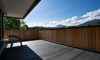 A beautiful balcony with wood paneling and a view of the mountains. The sky is clear and sunny with a few clouds.